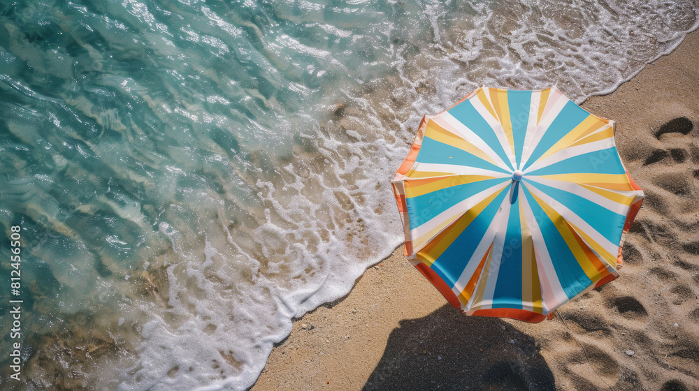 Naklejka premium A colorful striped beach umbrella stands out against the sandy shore and gentle waves.