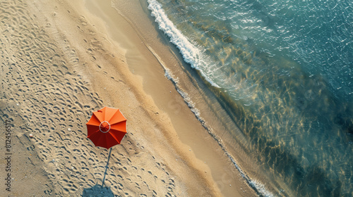 A solitary red umbrella on a sandy beach beside a tranquil sea at dawn.