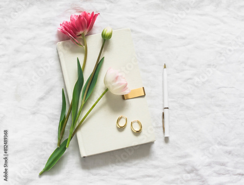 Tulips, a book, earrings, a pen on white sheets top view. Aesthetic still life