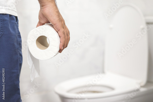 Man suffers from diarrhea hand hold tissue paper roll in front of toilet bowl. constipation in bathroom. Treatment stomach pain and Hygiene, health care © methaphum