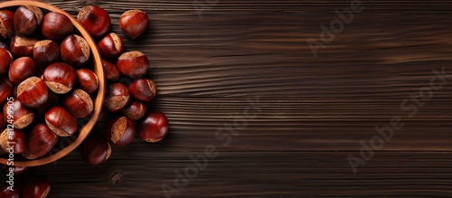 Top view of a wooden table with a bowl of roasted sweet chestnuts There is ample space available for text in the image