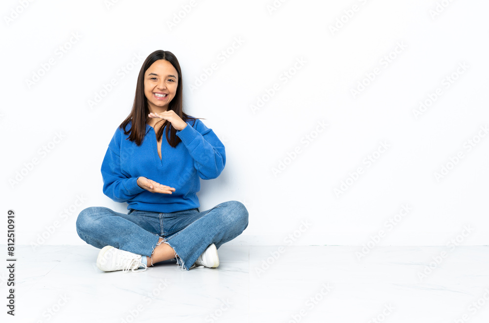Young mixed race woman sitting on the floor isolated on white background holding copyspace imaginary on the palm to insert an ad Young mixed race woman sitting on the floor isolated on white background holding copyspace imaginary on the palm to insert an ad