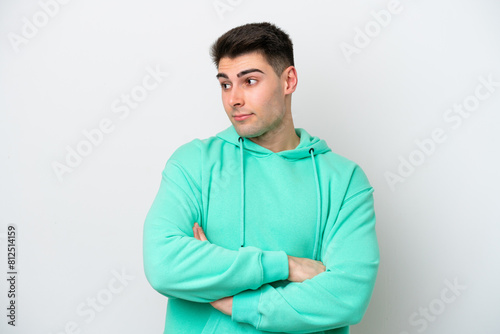 Young caucasian man isolated on white background making doubts gesture looking side © luismolinero