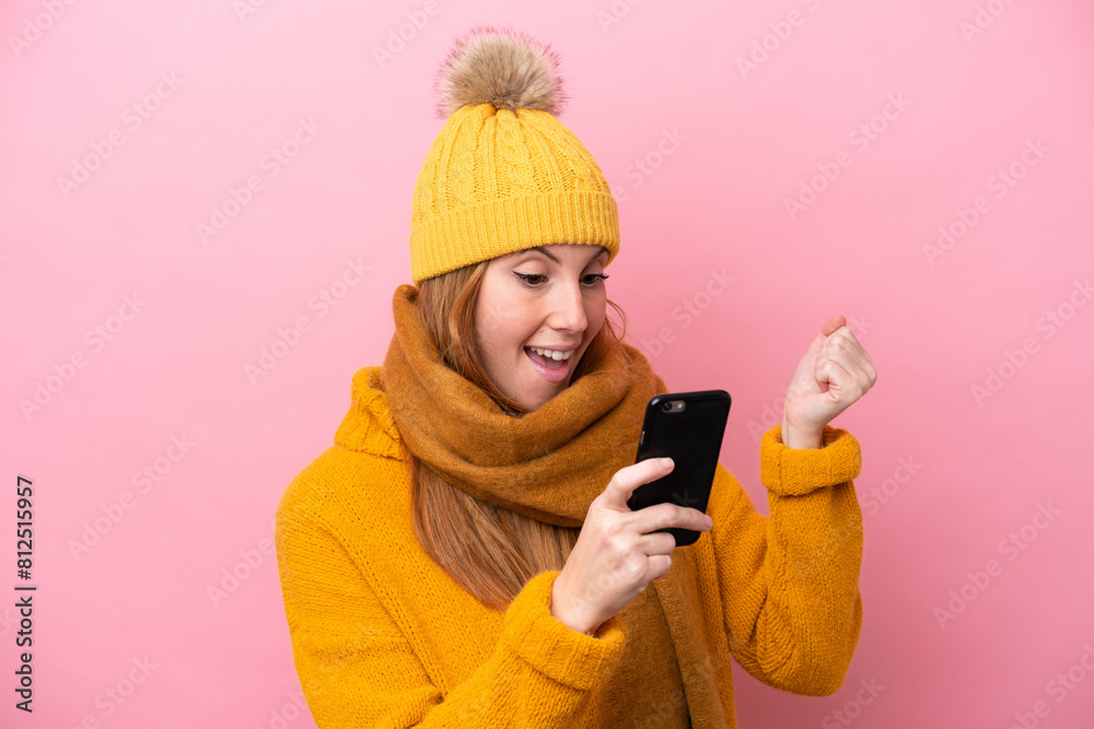 Young redhead woman wearing winter jacket isolated on pink background surprised and sending a message