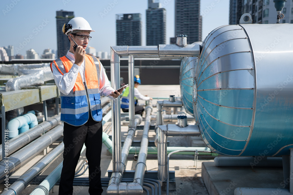 Portrait Asia male engineer in protective workwear is performing a conducts system check with use tablet computer and walkie talkie at rooftop building Portrait Asia male engineer in protective workwear is performing a conducts system check with use tablet computer and walkie talkie at rooftop building