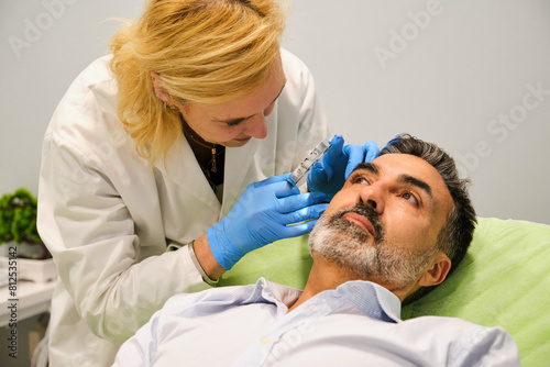 Aesthetic doctor is examining a man s face with a magnifying glass in a aesthetic clinic.