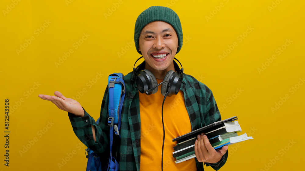 Confident Asian student in beanie and casual clothes, carrying backpack and headphones, Holding a stack of books. Isolated on yellow background. Academic success, preparation, or the joy of learning. Confident Asian student in beanie and casual clothes, carrying backpack and headphones, Holding a stack of books. Isolated on yellow background. Academic success, preparation, or the joy of learning.