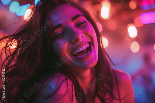 Attractive woman laughing at the camera, laughing at a party, with long dark hair, against a bokeh lights background at night time.