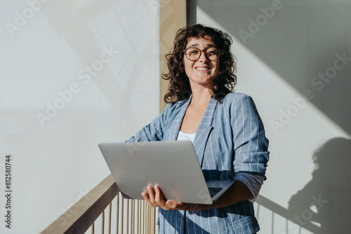 Cheerful businesswoman standing with a laptop on a balcony