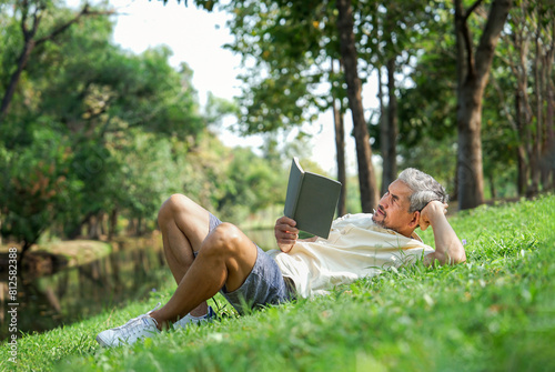 healthy senior man lying on grasses in the nature park,reading a book,mature male relaxing in the morning sunshine