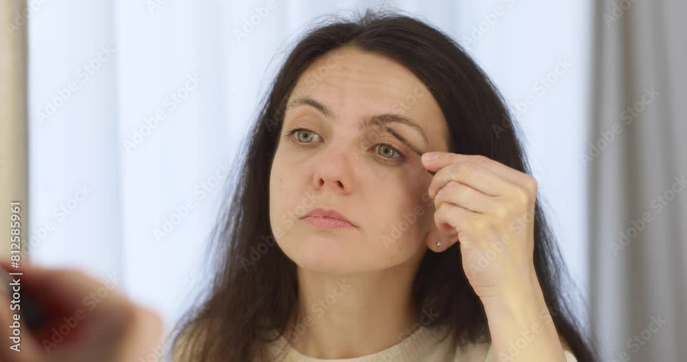 pretty woman brushing eyebrows with cosmetic brush and looking at mirror at home pretty woman brushing eyebrows with cosmetic brush and looking at mirror at home
