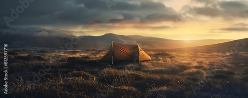 A lone tent sits in a vast field of grass  surrounded by mountains. The sky is a deep orange  and the sun is setting.