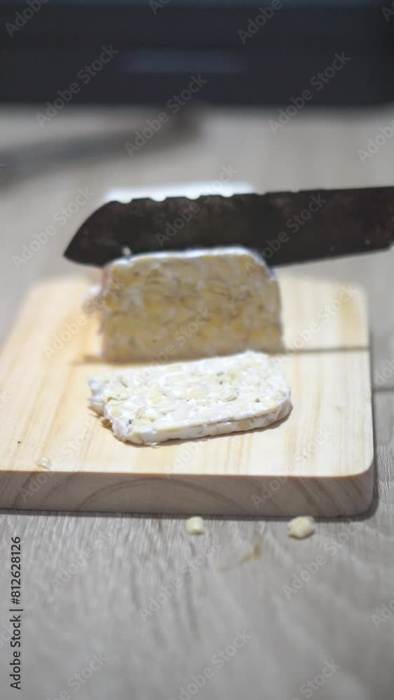 beautiful vertical video portrait,slicing tempeh with a kitchen knife on the table at night