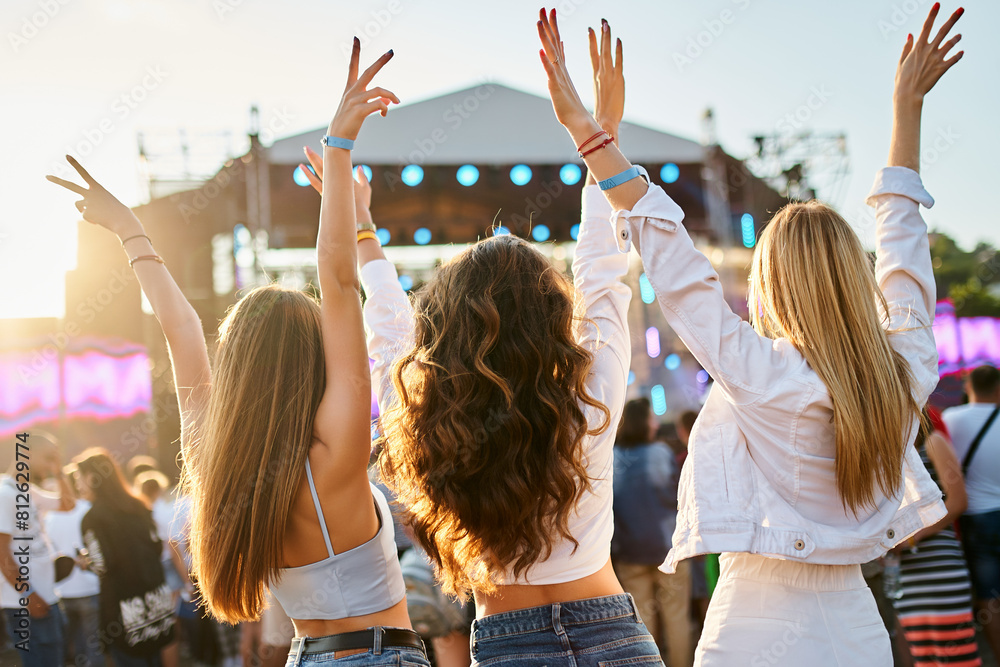 custom made wallpaper toronto digitalBack view of three young women at beach music festival, arms raised, dancing, enjoying summer sunset party vibe. Friends celebrate, fun outdoor event, casual fashion, stage lights in background.