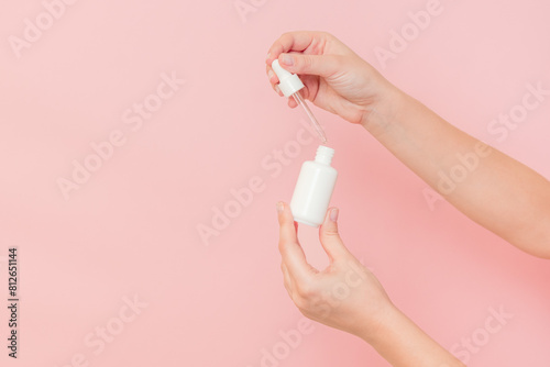 Hand holding glass cosmetic bottle for serum (hyaluronic acid and collagen) on pink background. Beauty concept © Anton Tolmachov