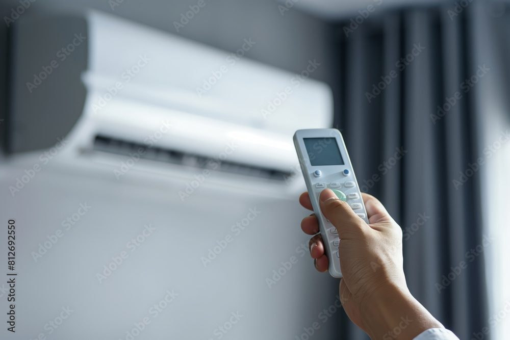 A hand holding a remote control pointing at an air conditioner on the wall. Shallow depth of field A hand holding a remote control pointing at an air conditioner on the wall. Shallow depth of field