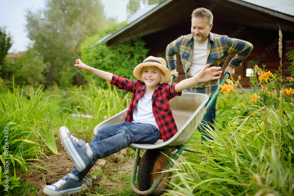 © Maria Sbytova - Wheelbarrow pushing by dad in domestic garden on warm sunny day. Active outdoors games for family with kids in the backyard © Maria Sbytova - Wheelbarrow pushing by dad in domestic garden on warm sunny day. Active outdoors games for family with kids in the backyard
