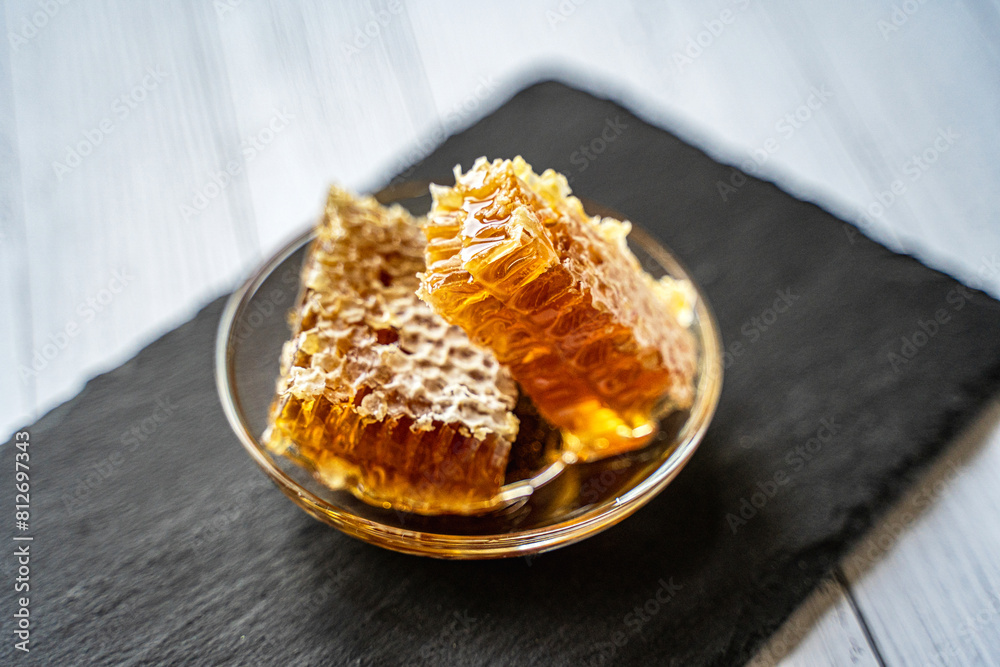 natural honey in a honeycomb, a juicy appetizing piece lies on a transparent plate on crumpled craft paper on a wooden background natural honey in a honeycomb, a juicy appetizing piece lies on a transparent plate on crumpled craft paper on a wooden background