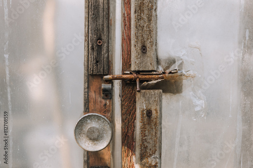 Photo of an old closed door with a latch of an oilcloth and wood greenhouse. photo