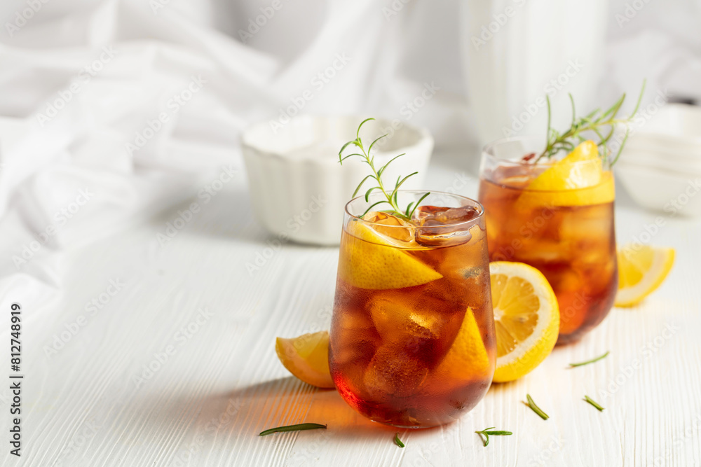 Iced tea or alcoholic cocktail with ice, rosemary and lemon slices on the white table. Iced tea or alcoholic cocktail with ice, rosemary and lemon slices on the white table.