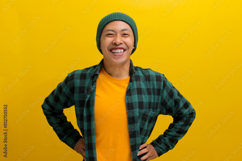 Confident young Asian man stands with a wide smile, his arms akimbo, exuding confidence as he faces the camera against a yellow background Confident young Asian man stands with a wide smile, his arms akimbo, exuding confidence as he faces the camera against a yellow background