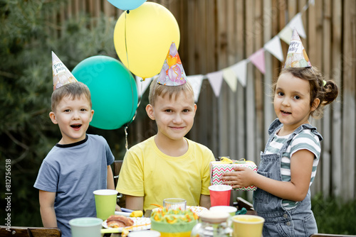 Cute funny nine year old boy celebrating his birthday with family or friends with homemade baked cake in a backyard. Birthday party for kids. He gets presents gift box.