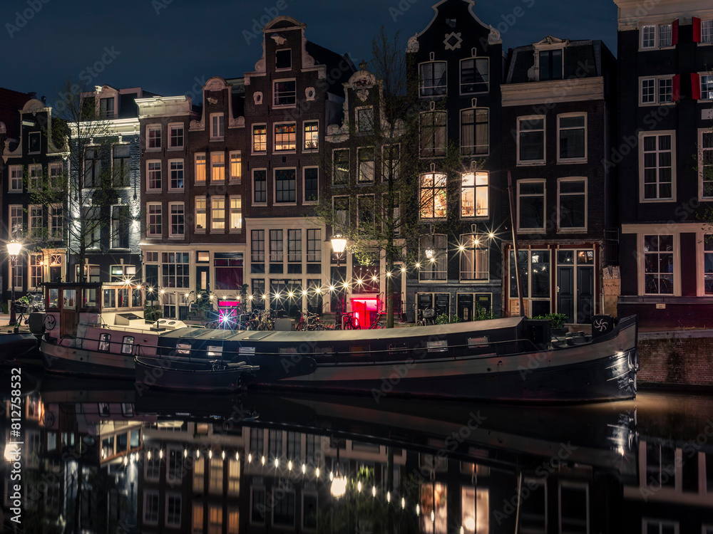 An illuminated houseboat reflecting in the Singel canal in Amsterdam at night
