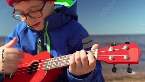 A happy school-age boy is having fun playing a small ukulele  photo