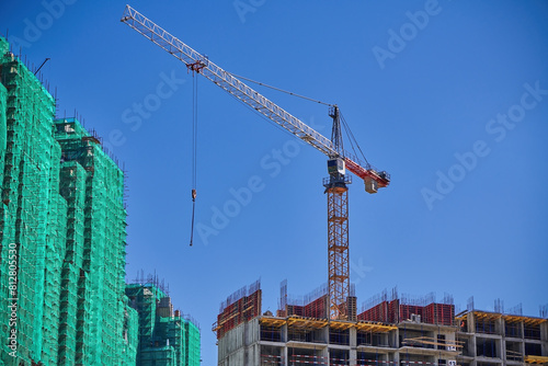 Tower crane on construction site against blue sky. Tall building under construction. Real estate construction. Concept of urban development and architecture.