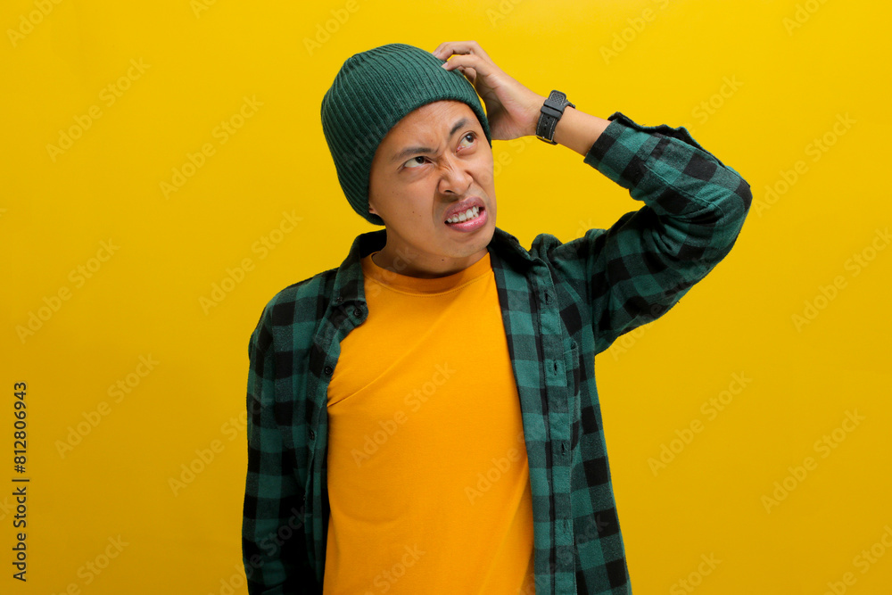 A puzzled young Asian man, dressed in a beanie hat and casual clothes, scratches his head while seeking a solution, portraying doubt and confusion, standing against a yellow background A puzzled young Asian man, dressed in a beanie hat and casual clothes, scratches his head while seeking a solution, portraying doubt and confusion, standing against a yellow background