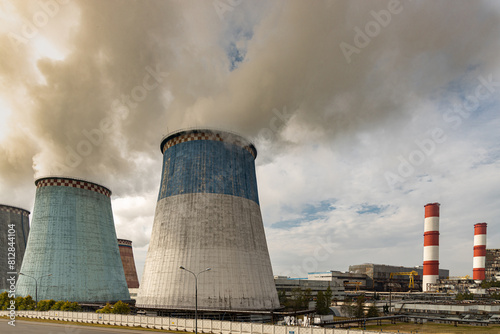 Large cooling towers of a fossil fuel powered electricity plant emitting pollution with the buildings and chimneys of the power station visible.