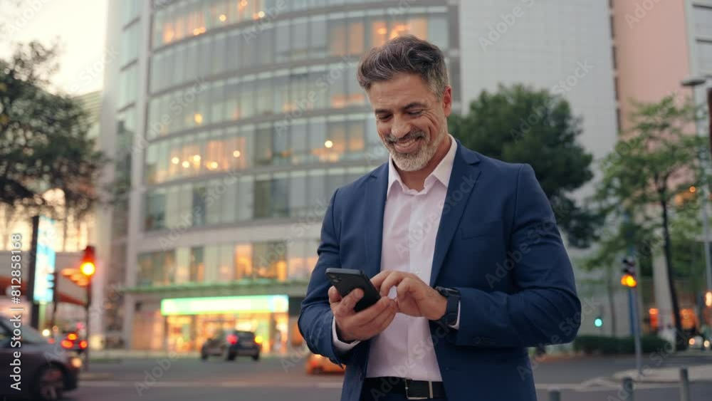 European latin middle age male entrepreneur businessman working on mobile cell phone. Confident mature hispanic senior business man holding smartphone cellphone, using app at busy street at evening