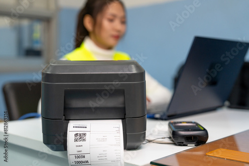 Beautiful Asian woman uses a laptop or notebook to print bar code stickers on a bar code printer. Selective focus at sticker barcode. photo