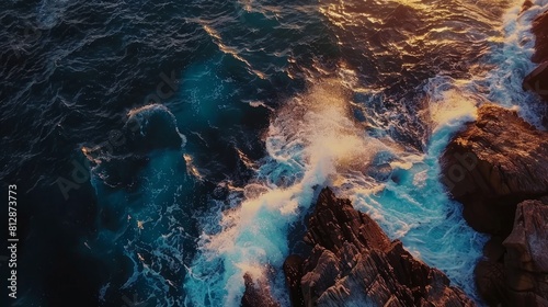 Spectacular drone photo, top view of seascape ocean wave crashing rocky cliff with sunset at the horizon as background. Beautiful coastal scenic landscape with turquoise water beating rocky boulder.