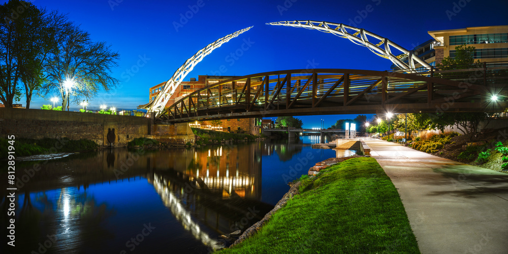 Fototapeta premium Sioux Falls Downtown River Greenway Lighted Trail, Skyline, Bridges, and Reflectoins on the Big Sioux River Water at Night in South Dakota, USA
