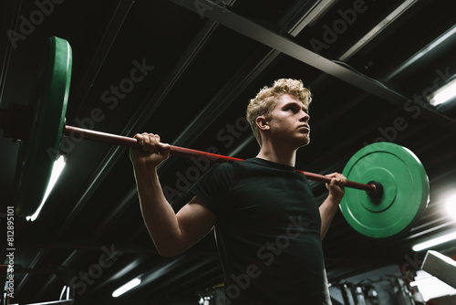 Low angle shot of a young strong male athlete exercising with a barbell with red weights