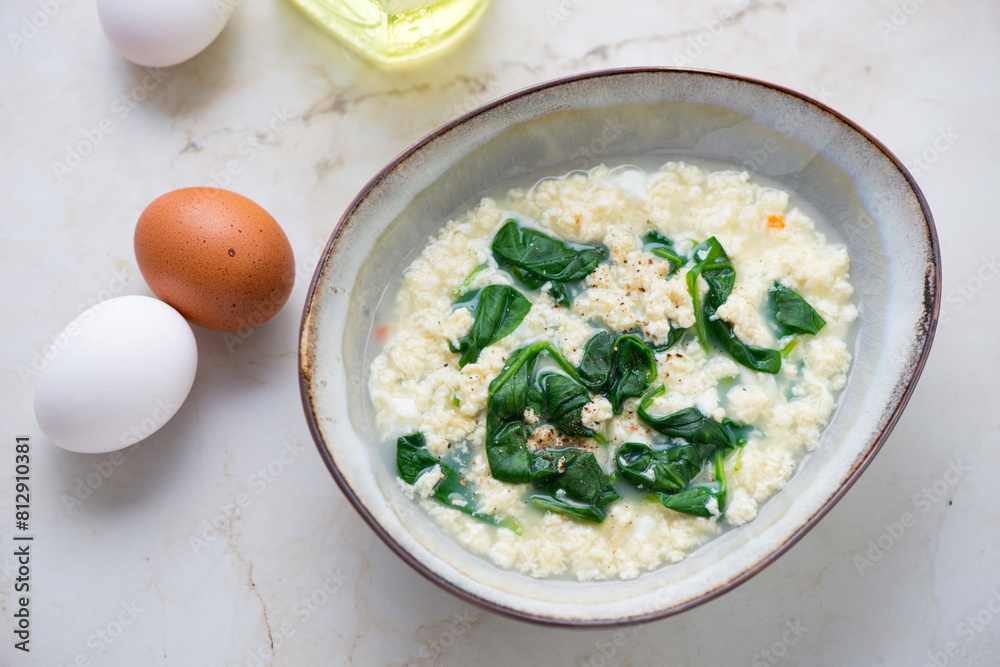 Bowl of stracciatella or egg-drop soup with spinach, horizontal shot on a light-beige marble background, high angle view Bowl of stracciatella or egg-drop soup with spinach, horizontal shot on a light-beige marble background, high angle view