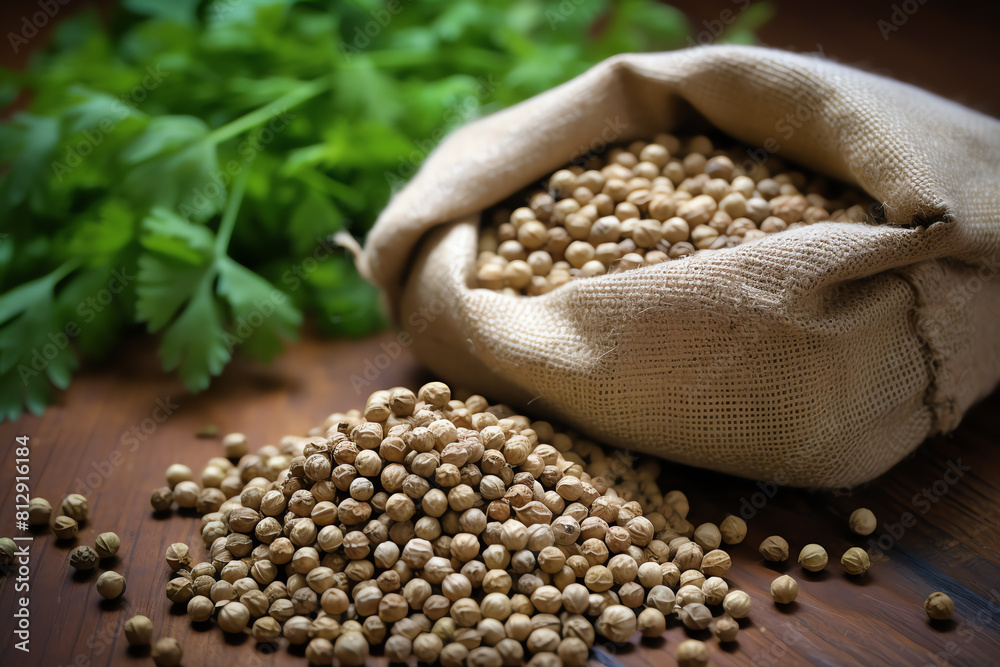 Obraz premium Coriander seeds scattered on a wooden surface, ready for planting or use in cooking, with a burlap sack partially open nearby