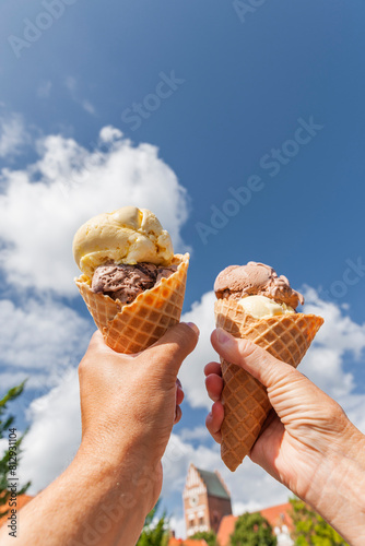 Eistüte mit Eiskugeln in der Hand vor blauem Himmel