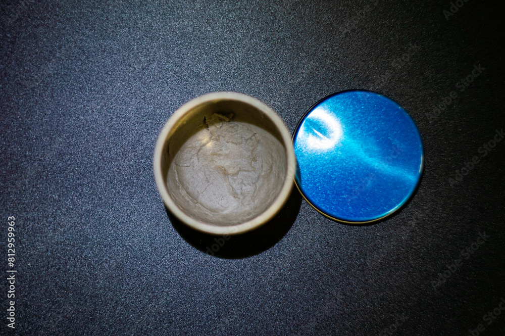 half empty gray paste in container with blue closure on black background highlighted half empty gray paste in container with blue closure on black background highlighted