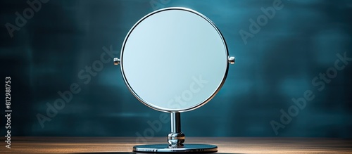 A round magnifying mirror with a handle made of chromed steel sits on a table against a background of cold light creating a clean and pure atmosphere The studio setting provides copy space for text o