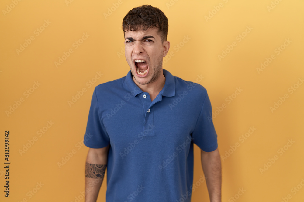 Young hispanic man standing over yellow background angry and mad screaming frustrated and furious, shouting with anger. rage and aggressive concept. Young hispanic man standing over yellow background angry and mad screaming frustrated and furious, shouting with anger. rage and aggressive concept.