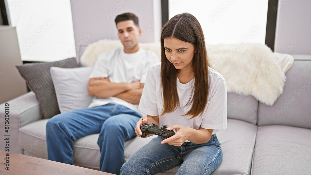 A focused woman plays a video game while a man lounges on the couch in a cozy living room setting A focused woman plays a video game while a man lounges on the couch in a cozy living room setting