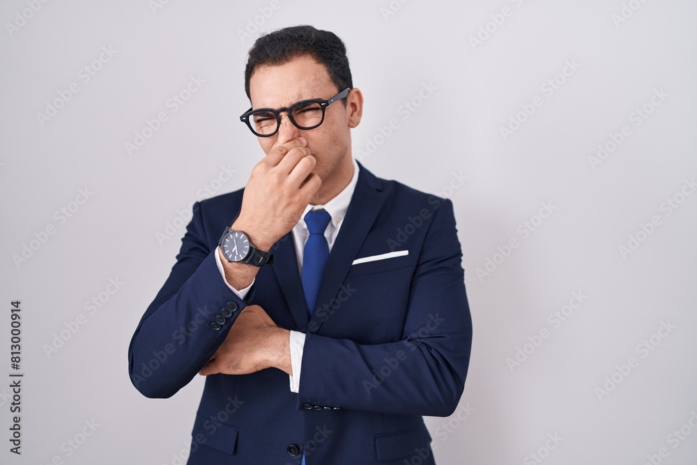 Young hispanic man wearing suit and tie smelling something stinky and disgusting, intolerable smell, holding breath with fingers on nose. bad smell Young hispanic man wearing suit and tie smelling something stinky and disgusting, intolerable smell, holding breath with fingers on nose. bad smell
