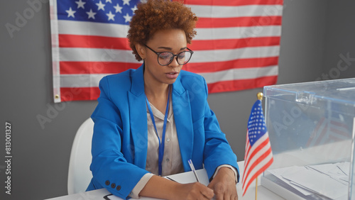 African american woman in a blue blazer taking notes indoors with an american flag in the background, portraying a professional electoral atmosphere. photo