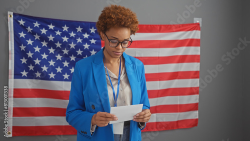 American black woman in blue jacket reading document indoors with us flag background.