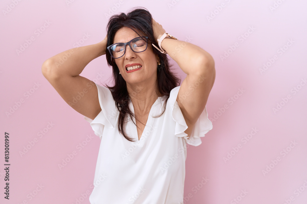 Middle age hispanic woman wearing casual white t shirt and glasses suffering from headache desperate and stressed because pain and migraine. hands on head.