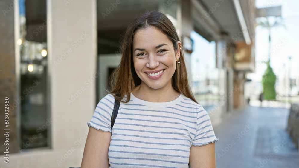 A smiling woman with blue eyes and brunette hair enjoys a sunny day outdoor in the city. A smiling woman with blue eyes and brunette hair enjoys a sunny day outdoor in the city.