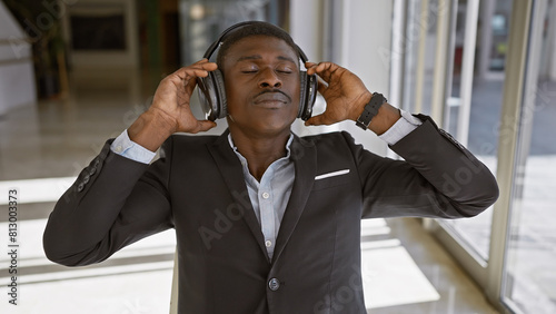 African businessman relaxing with headphones in a modern office setting, eyes closed and enjoying music.