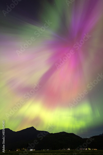 A vibrant aurora borealis dances in the night sky, displaying a mesmerizing blend of green, purple, and pink hues above a dark silhouette of a mountainous landscape © peteleclerc